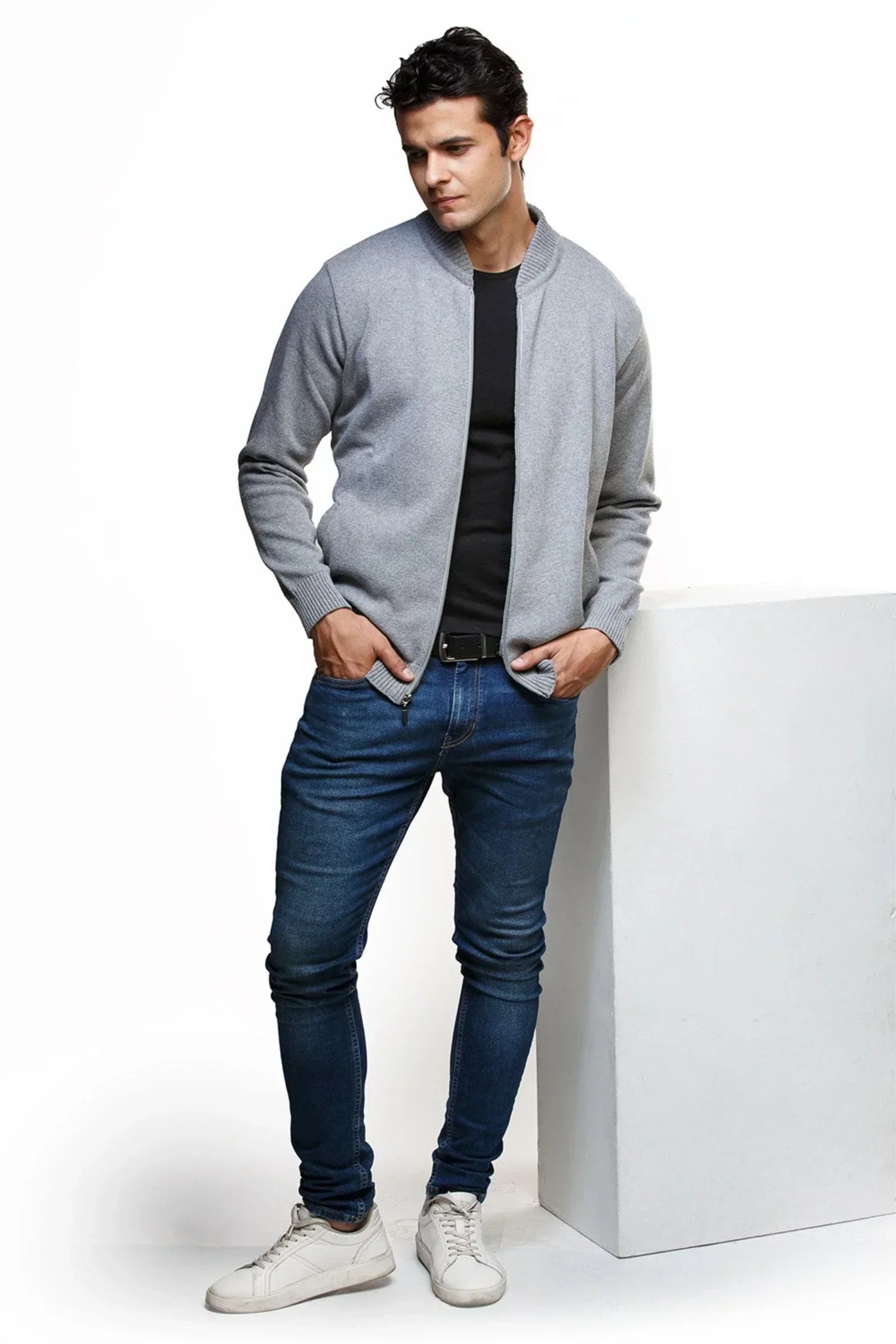 Hombre con chaqueta gris de tejido de punto, camiseta negra, jeans ajustados y tenis blancos
