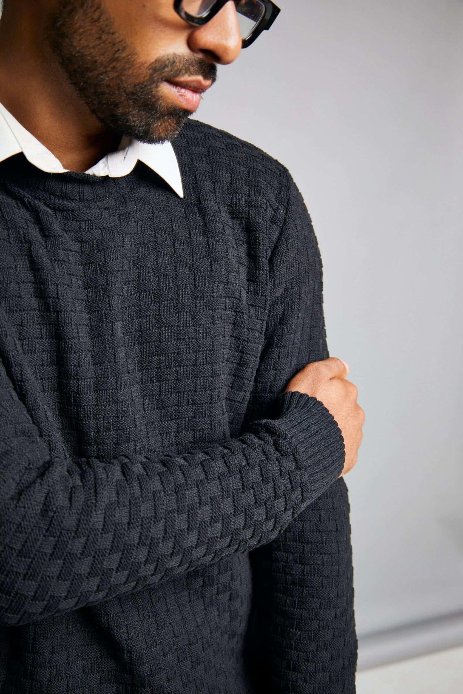 Hombre con suéter tejido de punto negro y camisa blanca, detalle de textura elegante