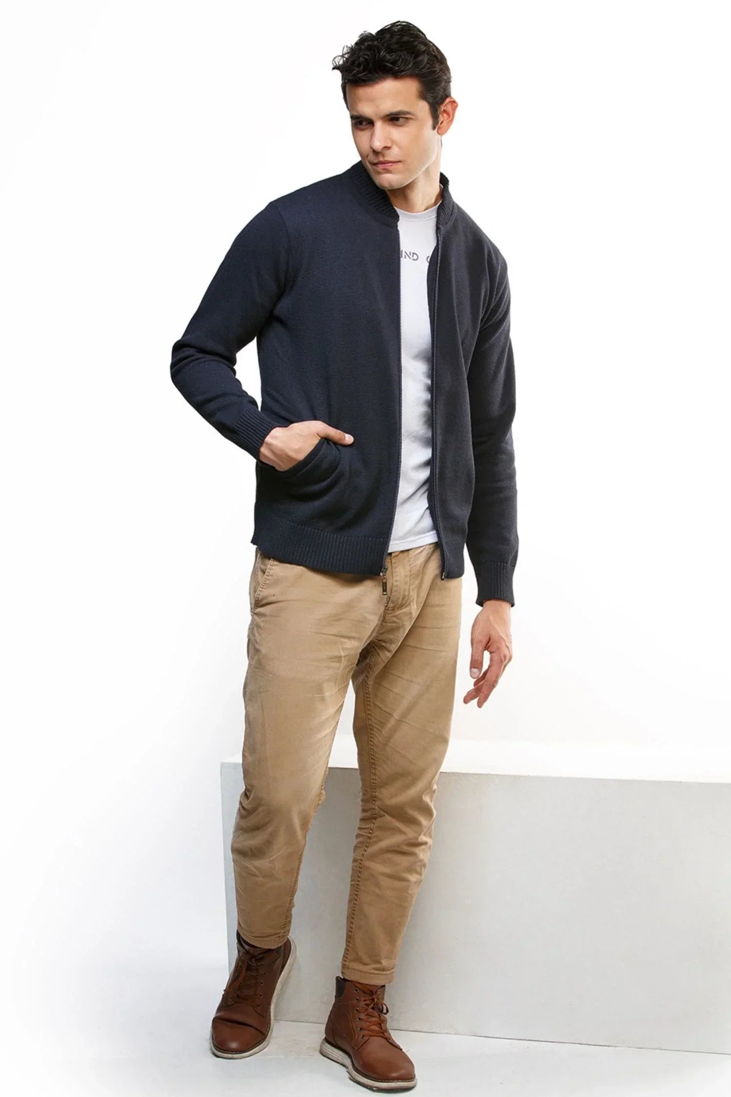 Hombre usando chaqueta azul marino de punto, camiseta blanca, pantalón beige y botas café