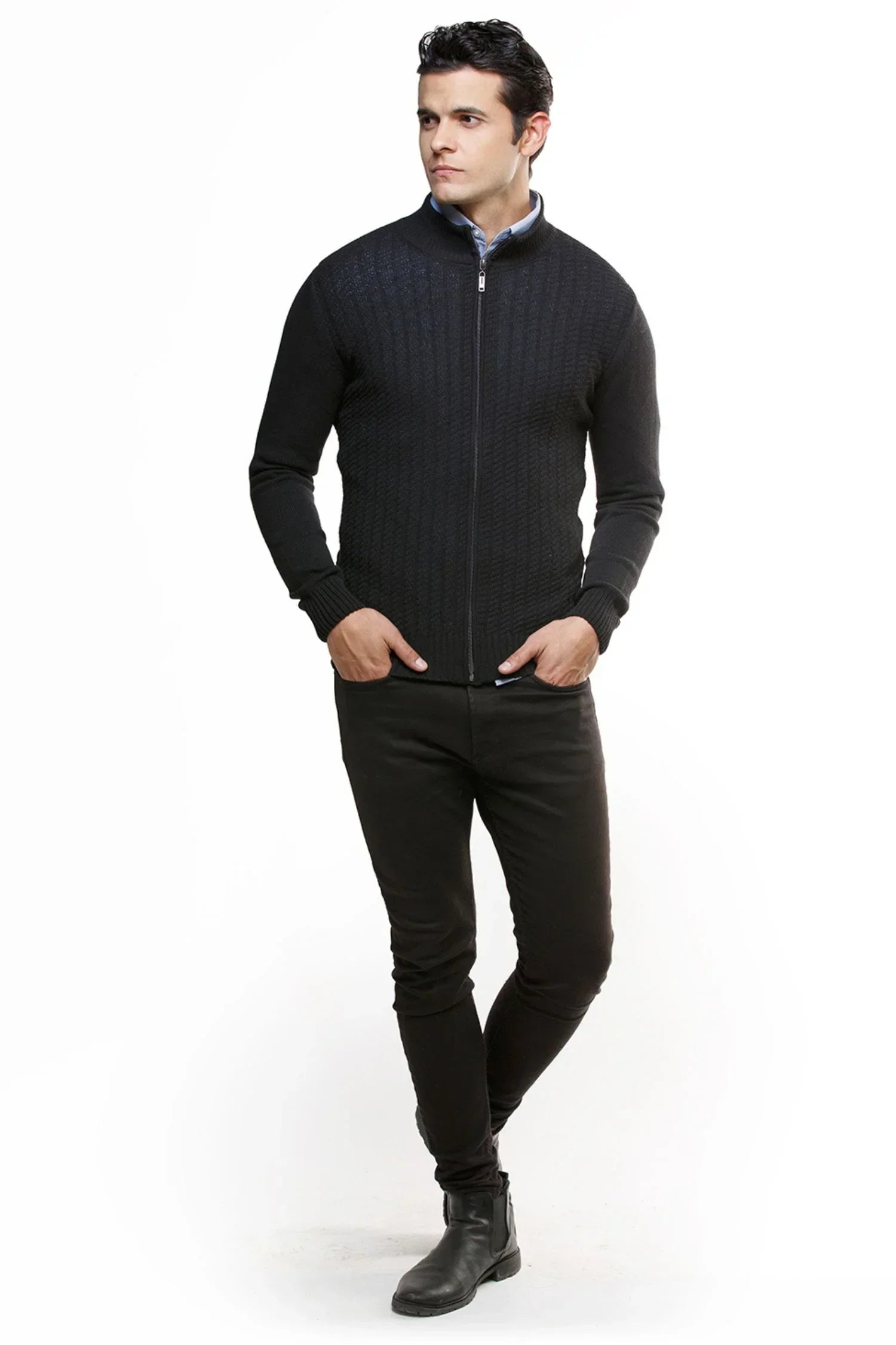 Hombre vistiendo chaqueta negra de punto con cierre, pantalón oscuro y botas, fondo blanco