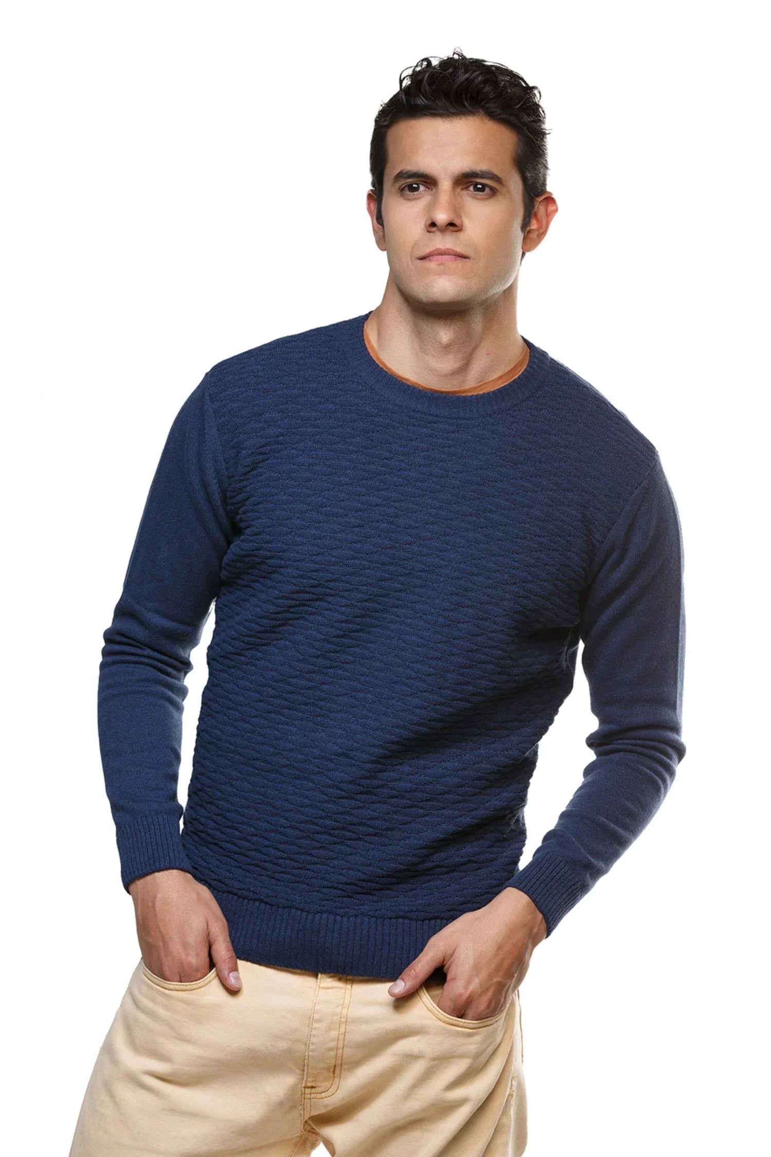 Hombre con suéter azul de punto manga larga y pantalón beige, fondo blanco, moda masculina.