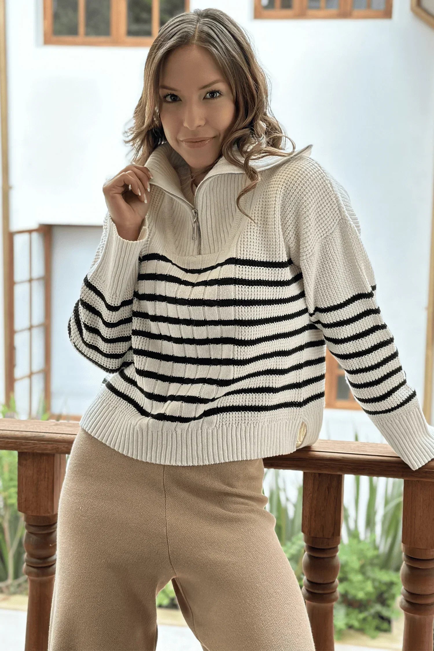 Mujer con suéter tejido de punto blanco y negro de rayas, pantalón beige, moda casual femenina