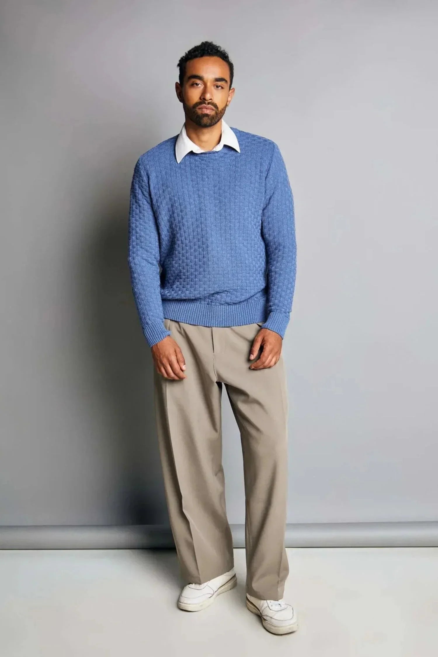 Hombre con suéter tejido azul, camisa blanca y pantalón beige, moda de punto para hombre