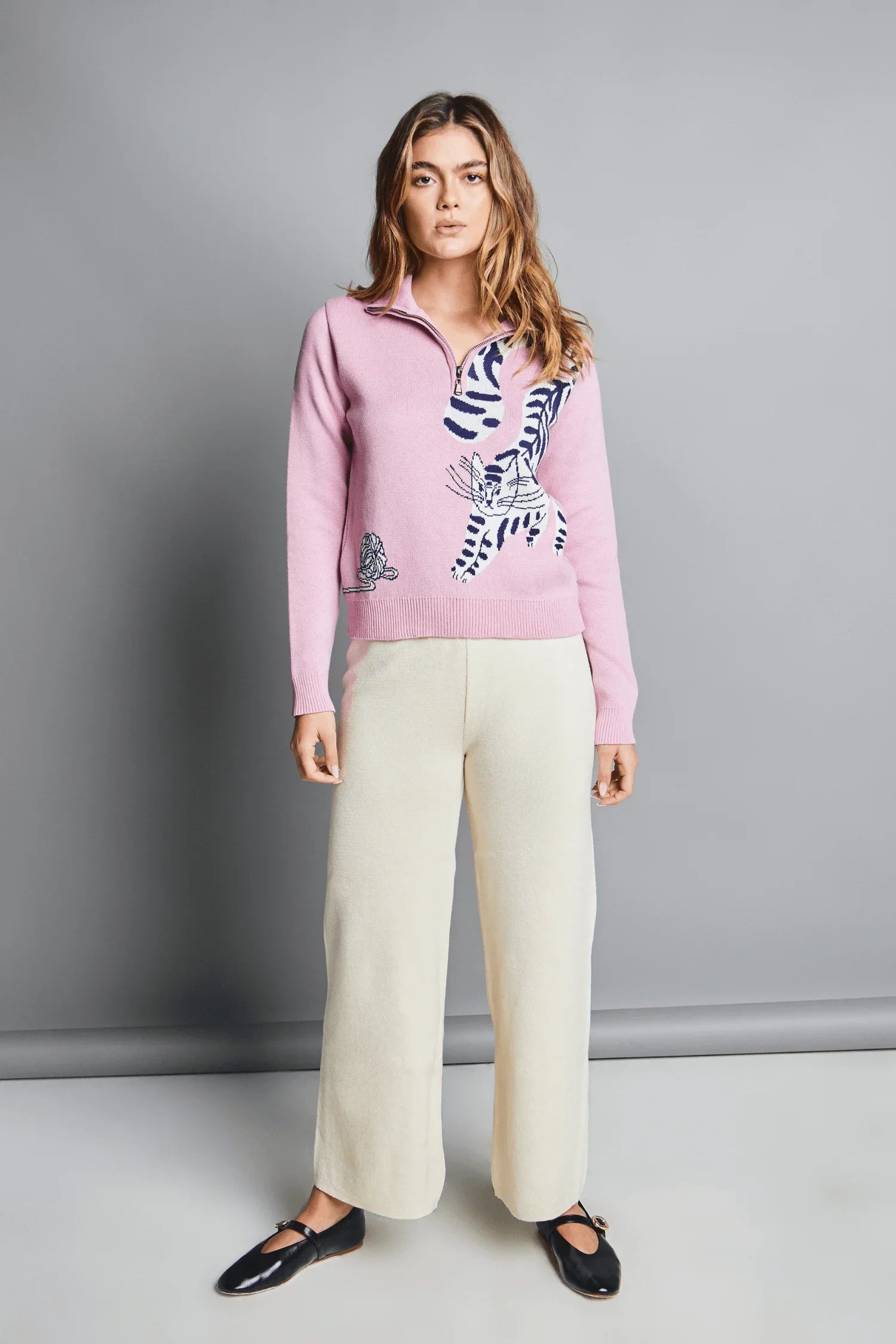 Mujer con suéter rosado tejido de punto con estampado de tigres y pantalón crema, moda femenina.