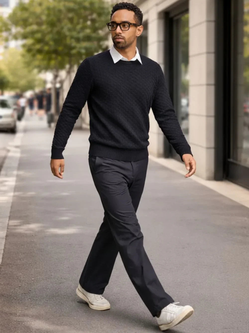 Hombre con suéter negro, camisa blanca y pantalón de punto caminando en la ciudad