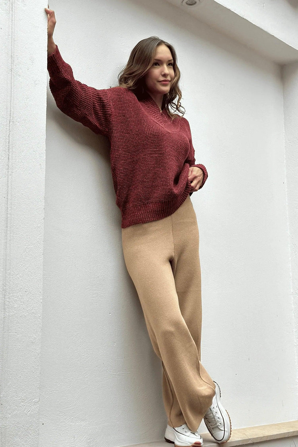 Mujer con suéter burdeos, pantalón beige y zapatillas blancas, estilo casual moderno.