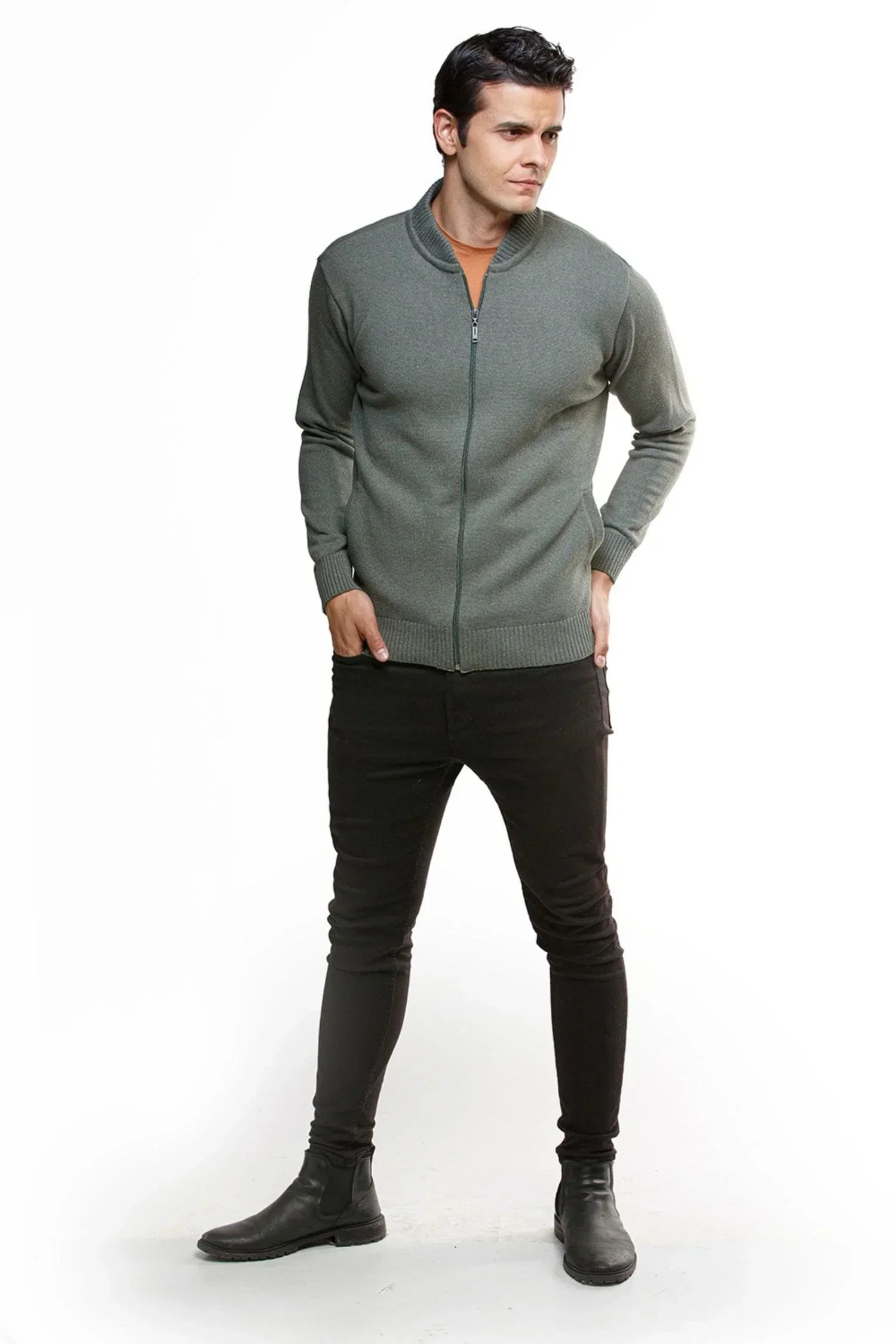 Hombre con chaqueta de punto gris, pantalón negro y botas negras, fondo blanco