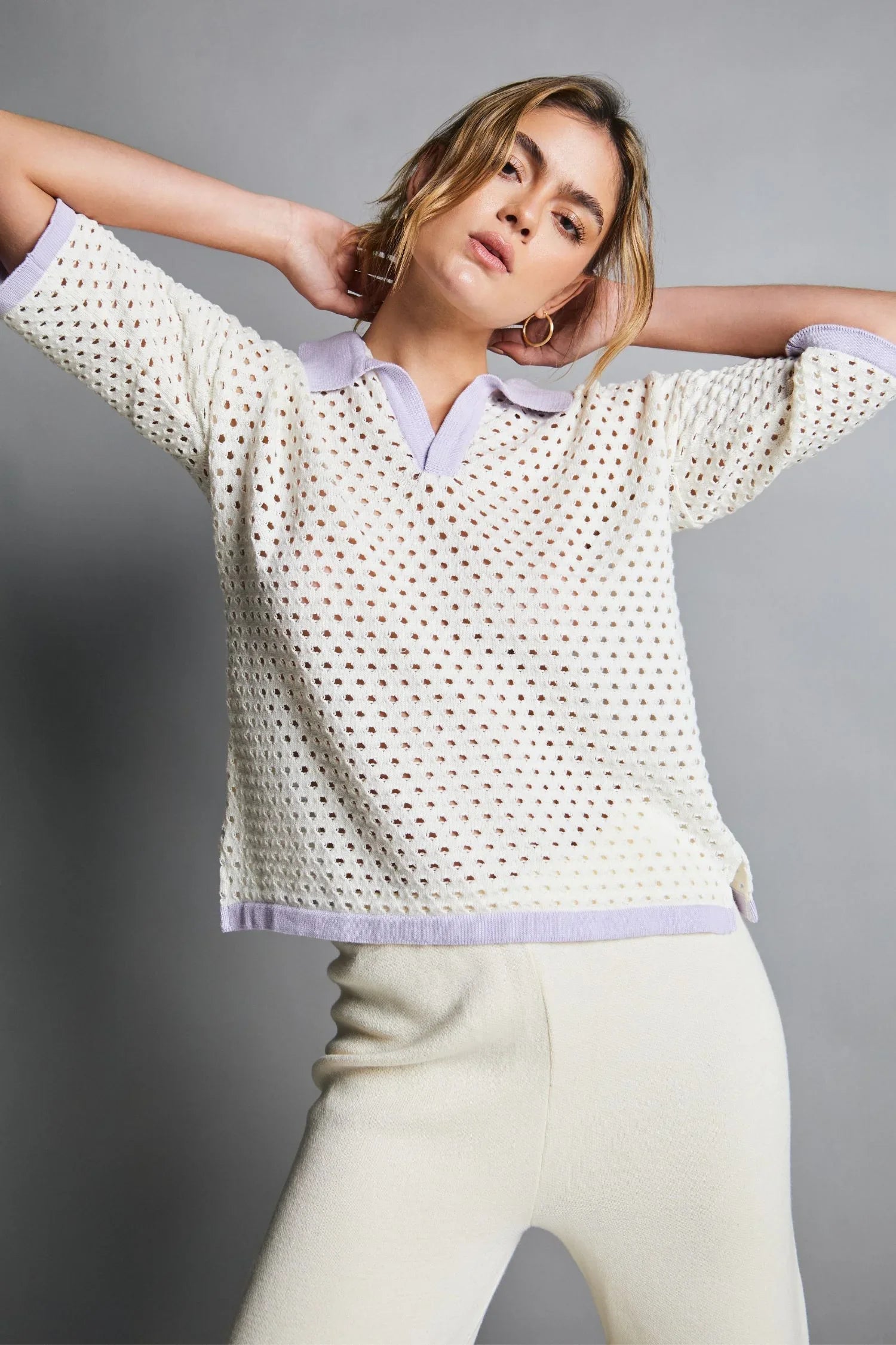 Mujer con blusa calada beige de punto y cuello lila, pantalón beige, moda femenina elegante