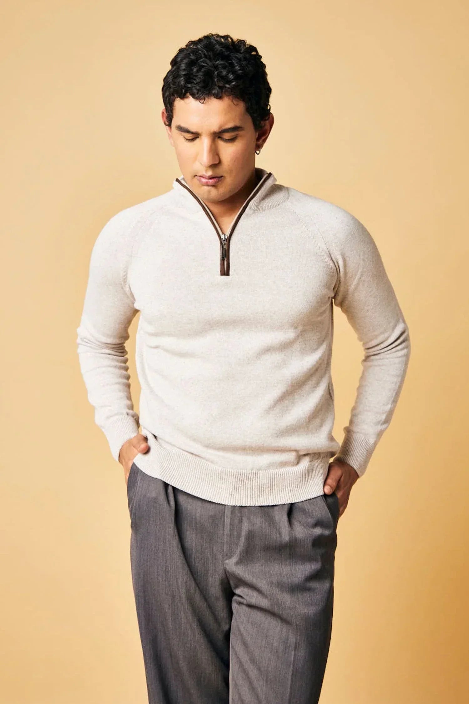 Hombre con suéter tejido beige de cremallera y pantalón gris, fondo beige, moda masculina