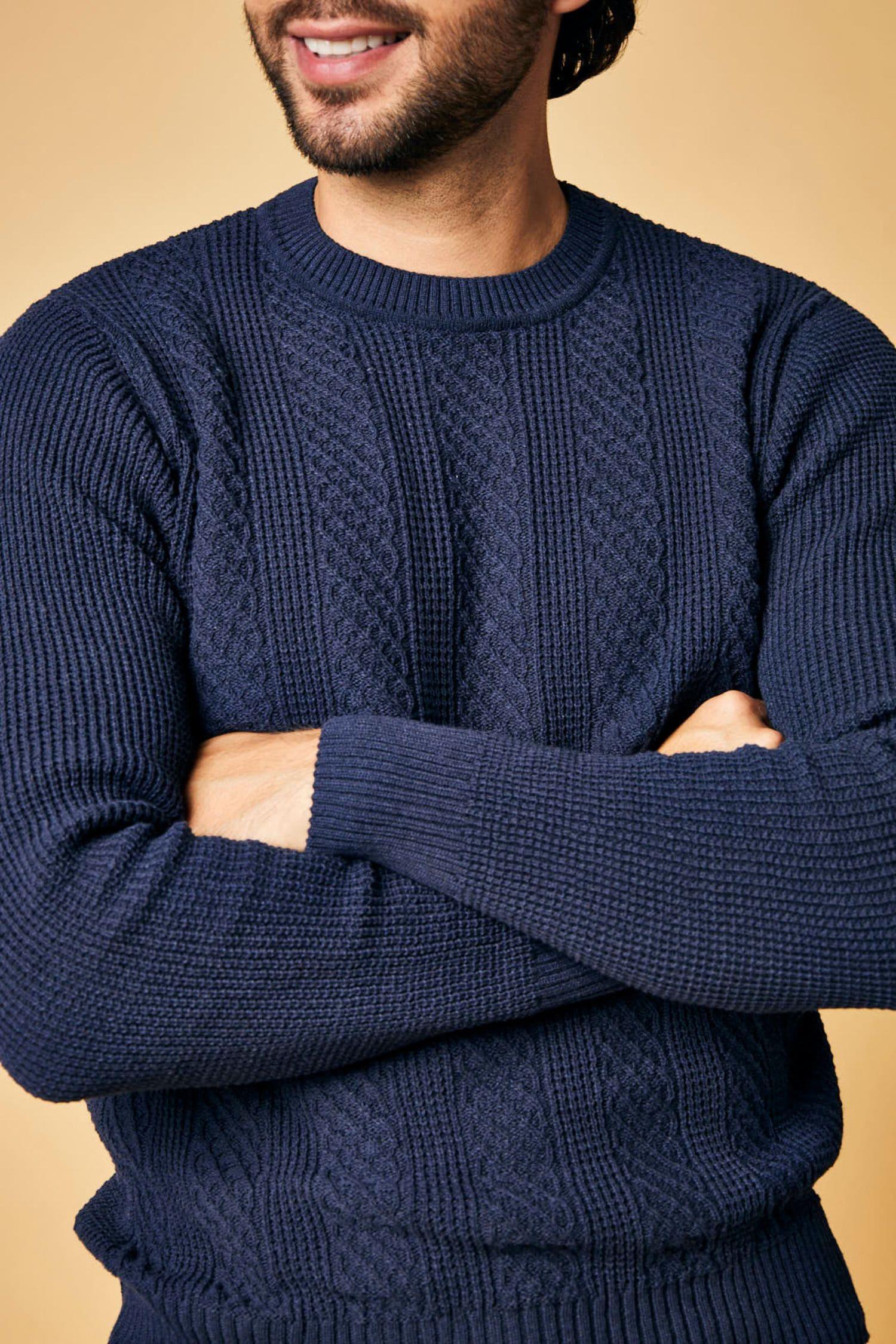 Hombre con suéter tejido azul marino de punto grueso, fondo beige, moda masculina.