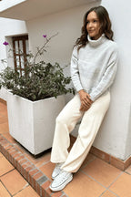 Mujer con suéter gris claro de cuello alto, pantalón crema y zapatillas blancas, estilo casual