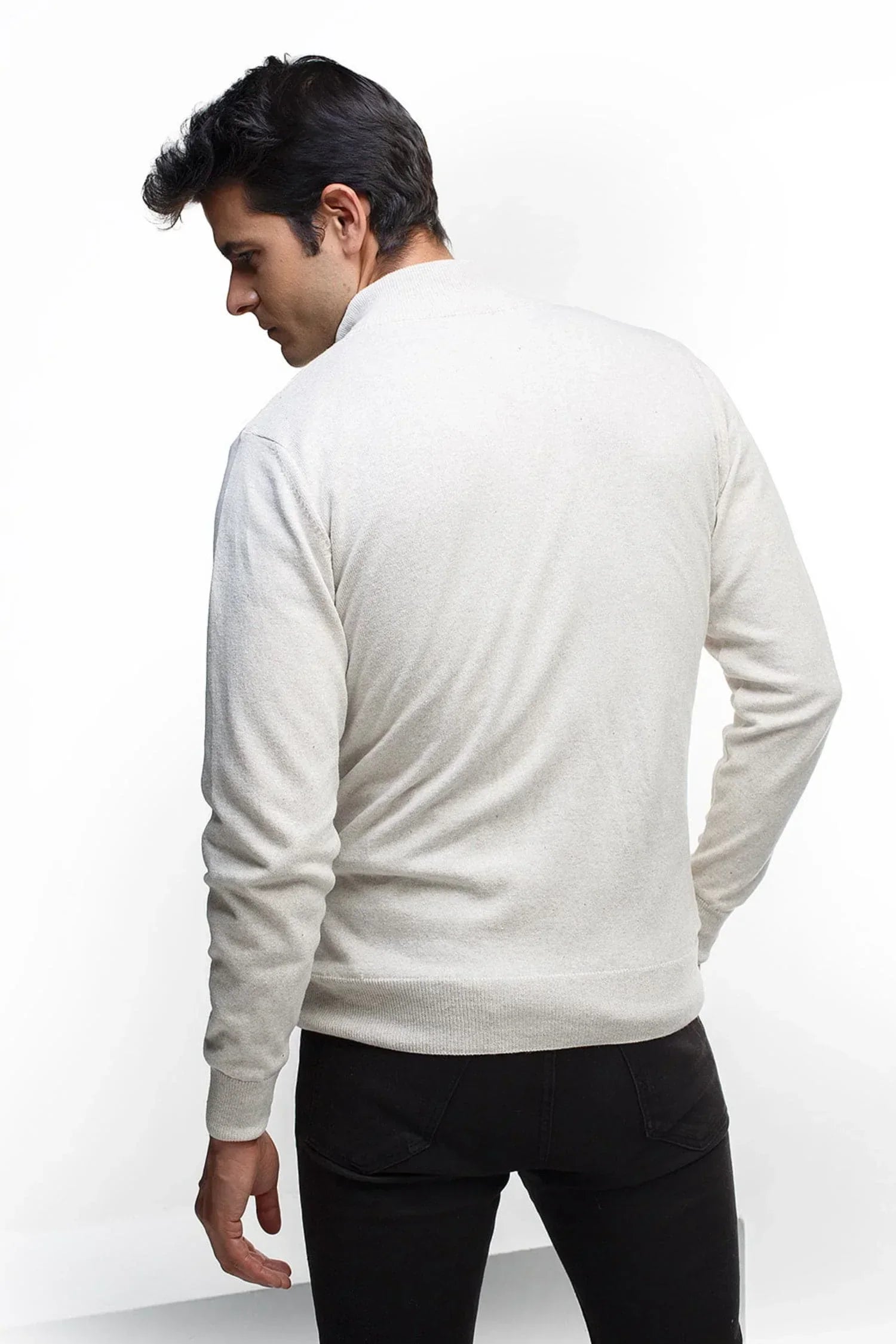 Hombre de espaldas con suéter de punto beige claro y pantalón negro en fondo blanco