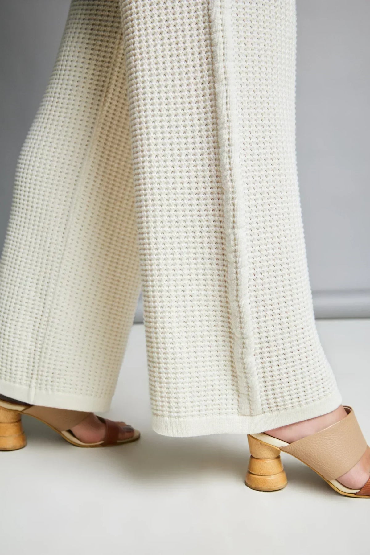 Pantalón tejido beige de pierna ancha y textura waffle, con sandalias de tacón madera.