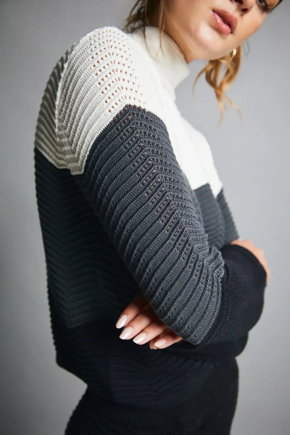 Suéter tejido de mujer en blanco, gris y negro, diseño moderno y textura acanalada.
