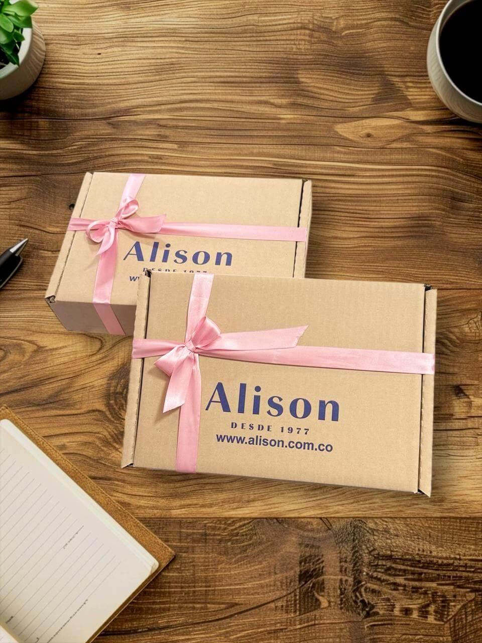 Cajas de regalo de cartón con cinta rosa y logo Alison sobre mesa de madera, ambiente acogedor